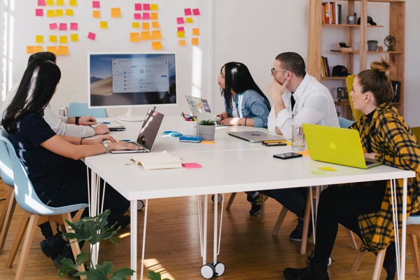Source: Unsplash. A team collaborates around a shared screen in a bright, modern office space, illustrating how the right technology and setup can support productive in-person work and enhance the return-to-office experience